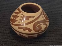 Round southwestern pottery jar with brown geometric designs on beige background