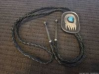 Full view of bolo tie showing braided leather cord and sterling silver slide with turquoise and bear claw design