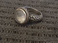 Front side angle showing clear cabochon gemstone in a 14k gold bezel with detailed filigree silver band.