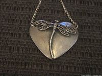 Close-up of the front of the heart pendant showing the detailed dragonfly design on a brushed sterling silver surface.