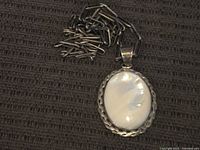 Front view of the oval mother of pearl pendant with silver chain on a textured surface