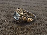 Close-up side view showing ornate sterling silver design and gold-toned divets with light blue faceted rectangular gemstone centerpiece.