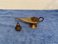 Photo showing two brass decorative lamps resembling Aladdin's lamp on a blue cloth, one larger with a removable lid and pedestal base, the other smaller with a removable conical lid.