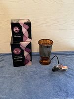 Amber fluted Scentsy wax warmer shown with two stacked boxes labeled Lampshade Collection Amber Fluted Shade and power cord wrapped beside warmer.