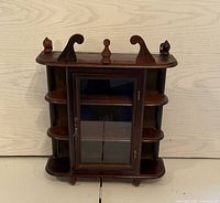 Front view of the antique dark wood display cabinet showing glass door, side shelves, and decorative top.