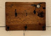 Wooden coat rack made from an antique oak school desktop, showing the front surface with five iron hooks and some darkened areas of wood.