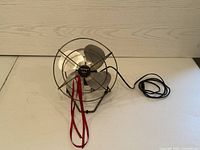 Front view of the Torcan small metal fan showing four metal blades inside a protective cage and power cord laid beside it.
