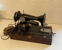 Antique Veritas sewing machine in detail, showing black body with gold decorative accents, motor, foot pedal, and logo plate.