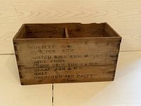 Front side view of the antique wooden box showing black stenciled text and internal divider.