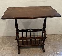 Front view of antique dark wood magazine rack showing flat top, turned legs, and vertical slatted magazine holder base.