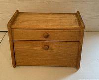 Front closed view of vintage wooden bread box with small drawer and drop-down front door.