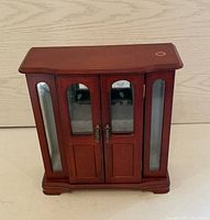 Closed cherrywood jewellery box showing front panel with two wooden and glass inset doors and glass panels on each side.