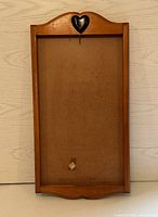 Front view of wooden rectangular calendar display with heart cutout at top and hook below, showing plain backboard.