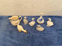 Seven ceramic goose collectibles including small pitcher, small vase, and six figurines displayed on blue towel
