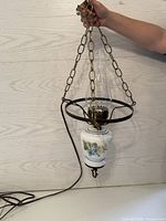 Photo of hanging electric lantern style lamp showing white glass base with blue floral pattern held by chain and metal frame with attached cord.