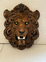 Front view of the handcrafted wooden lion head plaque showing detailed mane, yellow eyes, open mouth with white teeth.