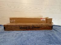 Natural wood gallery frame front close-up showing "Moments & Memories" inscription with packaging box behind.