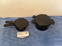 Front view of small and large black Pampered Chef microwave steamer pots with vented lids on blue towel with a Pampered Chef tag in front