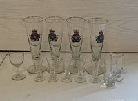 Four tall RCAF glasses featuring Royal Canadian Air Force emblem with gold rims along with ten smaller clear glasses of various styles displayed in front of a white wall.
