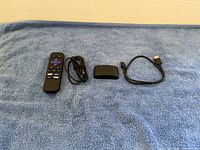 Photo showing Roku remote, power adapter cable, Roku Express device, and HDMI cable lined up on a blue towel.