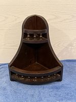 Front view of the small dark wood corner shelf showing three shelves and carved accents.
