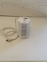 Small white electric bug zapper with multiple protective grills and plug-in power cord displayed on light surface.