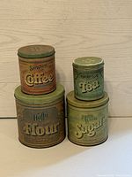 Vintage tin canister set of four showing labels for coffee, tea, flour, and sugar with clear aged wear and patina.