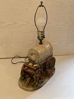 Front angle view of vintage covered wagon lamp with detailed ceramic base, exposed bulb, and metal harp for lampshade