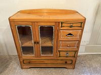 Front view of vintage wooden hutch showing two glass-paned doors, four small drawers on the right, and one large drawer at the bottom with handpainted green decorative accents.