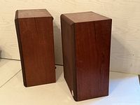 Two vintage wood box speakers shown from rear and side angles, with visible wood grain finish.