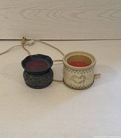 Two electric wax melting pots side-by-side on white surface, showing cords and wax melts inside each pot