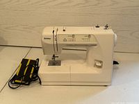 White Kenmore sewing machine with attached foot pedal, placed on tiled floor in front of a light wood wall.
