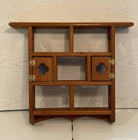 Front view of wooden display shelf showing two small doors with quatrefoil cut-outs, multiple open compartments, and flat top shelf.
