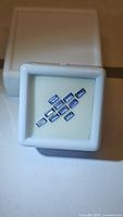 Ten rectangular baguette cut cornflower blue sapphires displayed in a white cushioned jewelry box.