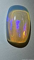 Close-up photo of 2.98ct natural Ethiopian opal showing electric purple and orange play-of-color on a pale translucent body with smooth polished surface.