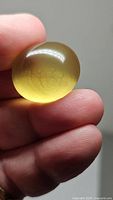 Close-up photo of a large natural lemon citrine oval cabochon held between fingers showing the stone's translucent yellow color and smooth polish.
