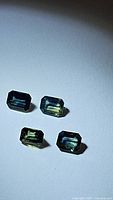 Four emerald cut multicolored sapphires with visible bicolored yellow and blue hues on white background