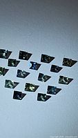 Photo showcasing 16 natural princess cut sapphires of varying green hues arranged in rows.