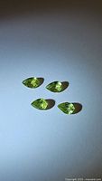 Four pear shaped apple green peridot gemstones on a white background captured with direct lighting to show color and clarity.