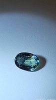 Close-up image of natural blue sapphire gemstone showing oval faceted cut and greenish-blue color.