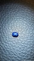 Oval cabochon blue star sapphire with a clear six-ray star effect on textured dark surface, under light to reveal star phenomenon.
