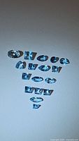 Top view of 14 natural blue topaz gemstones of mixed cuts arranged in triangular pattern on white background.