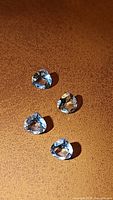 Four pear-shaped natural blue topaz gemstones arranged on brown surface showing their size, shape, and clarity.