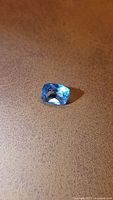 Natural cushion cut sky blue aquamarine gemstone lying on a brown textured surface showing its deep blue color and cushion shape.