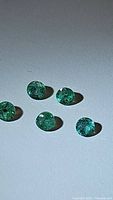 Photo showing five round cut natural Columbian emeralds laid out on a white background under soft lighting, highlighting their green color and faceted cuts.