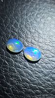 Two oval cabochon cut natural untreated Ethiopian opals showing vibrant play of color on textured black background under bright lighting.