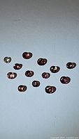 13 oval sapphire gemstones in shades of pink and padparadscha on flat surface