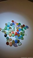 Photo of assorted natural mixed gemstones in various colors and shapes scattered on white background, showing overall parcel contents.