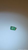 Close-up photo of rectangular emerald cut green emerald gemstone on plain background, showing color and clarity.