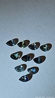 Ten natural pear shaped multicolored sapphires arranged on a white surface, showing colors ranging from blue to green.
